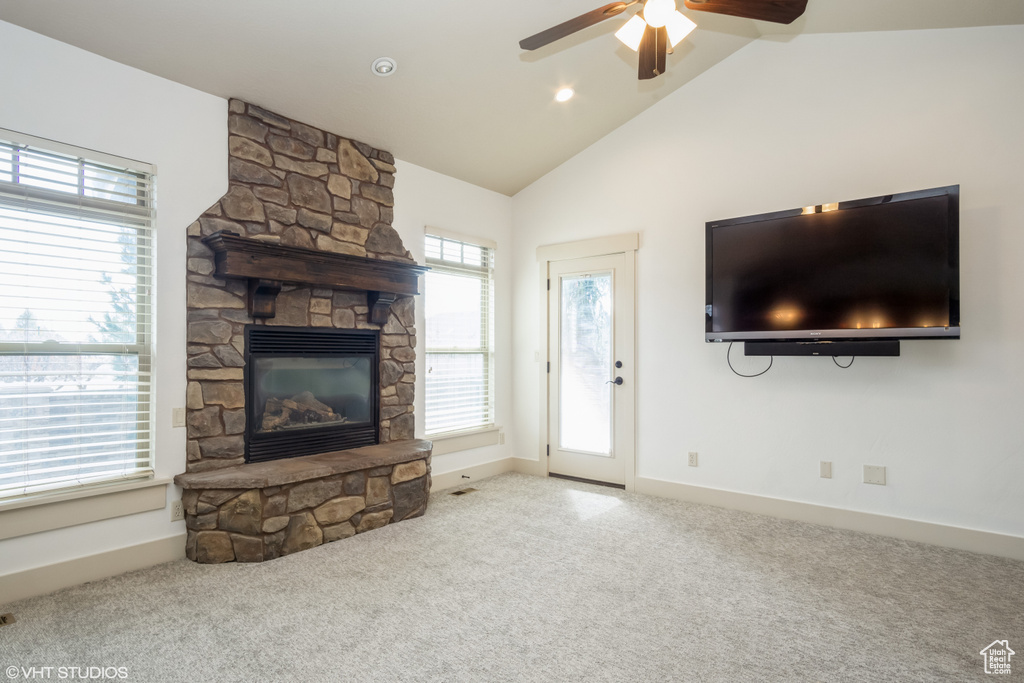 Unfurnished living room with light colored carpet, lofted ceiling, ceiling fan, and a stone fireplace