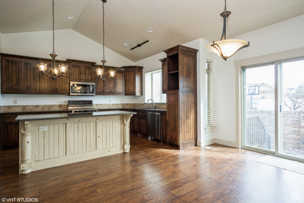 Kitchen featuring appliances with stainless steel finishes, dark wood-type flooring, a center island, and decorative light fixtures