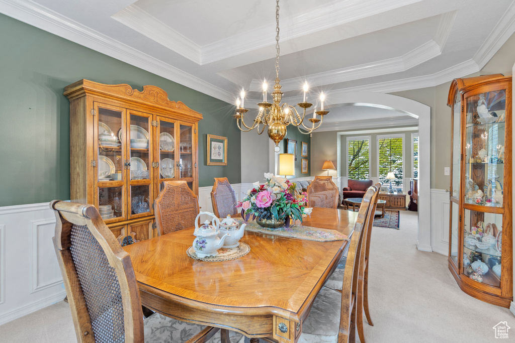 Dining space featuring ornamental molding, an inviting chandelier, light colored carpet, and a tray ceiling