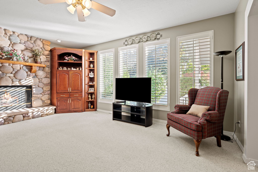 Living area featuring a stone fireplace, light colored carpet, and ceiling fan