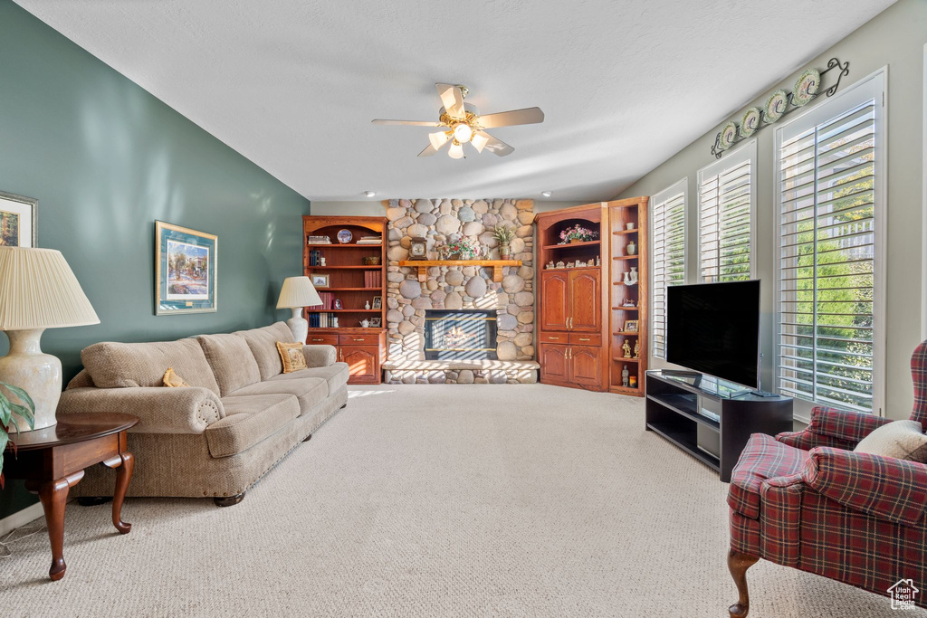 Living room with light colored carpet, ceiling fan, built in features, and a stone fireplace