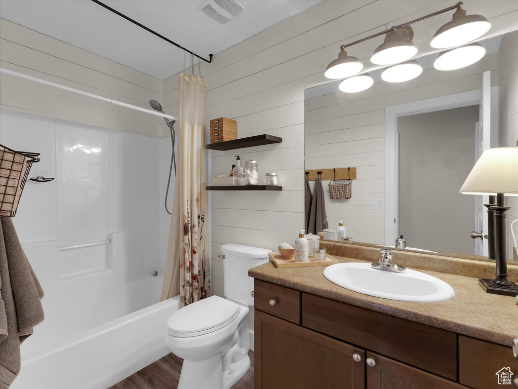 Full bathroom with shower / bath combo with shower curtain, wooden walls, toilet, vanity, and hardwood / wood-style flooring