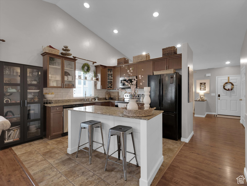 Kitchen featuring stone counters, appliances with stainless steel finishes, backsplash, light hardwood / wood-style floors, and a breakfast bar