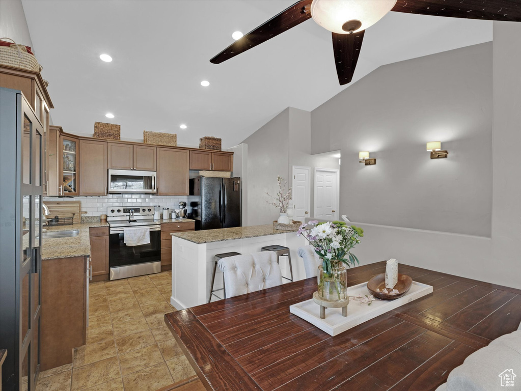 Kitchen with backsplash, vaulted ceiling, fridge, light stone counters, and range with electric cooktop