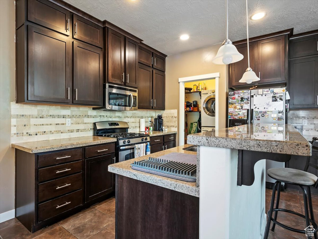 Kitchen with appliances with stainless steel finishes, a kitchen bar, backsplash, washer / clothes dryer, and pendant lighting