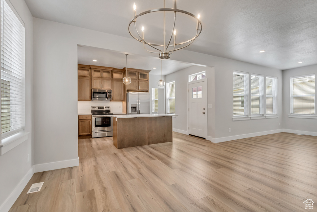 Kitchen featuring appliances with stainless steel finishes, a center island, pendant lighting, and light hardwood / wood-style floors