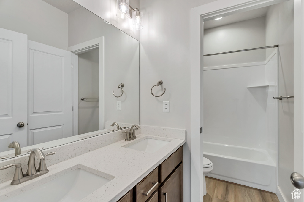 Full bathroom with vanity with extensive cabinet space, shower / bathing tub combination, hardwood / wood-style floors, double sink, and toilet