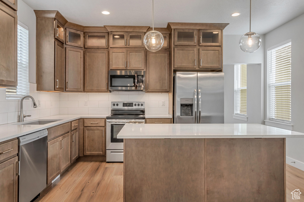 Kitchen featuring appliances with stainless steel finishes, light hardwood / wood-style flooring, tasteful backsplash, sink, and a center island