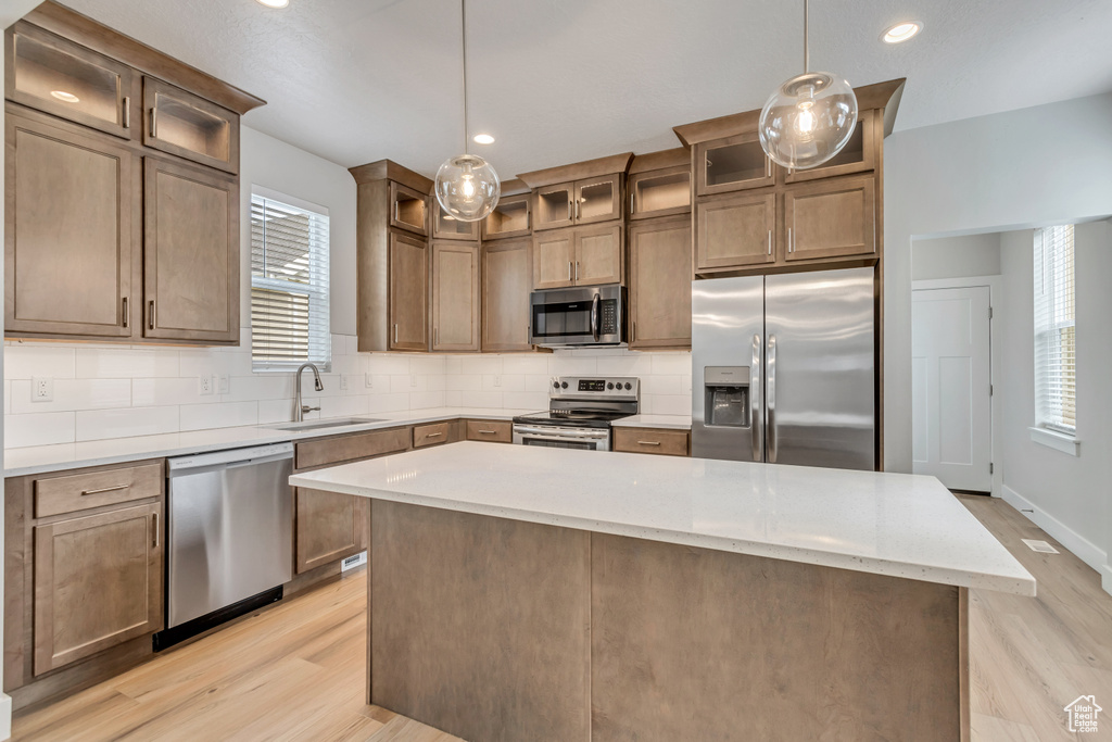 Kitchen featuring appliances with stainless steel finishes, a kitchen island, sink, backsplash, and decorative light fixtures