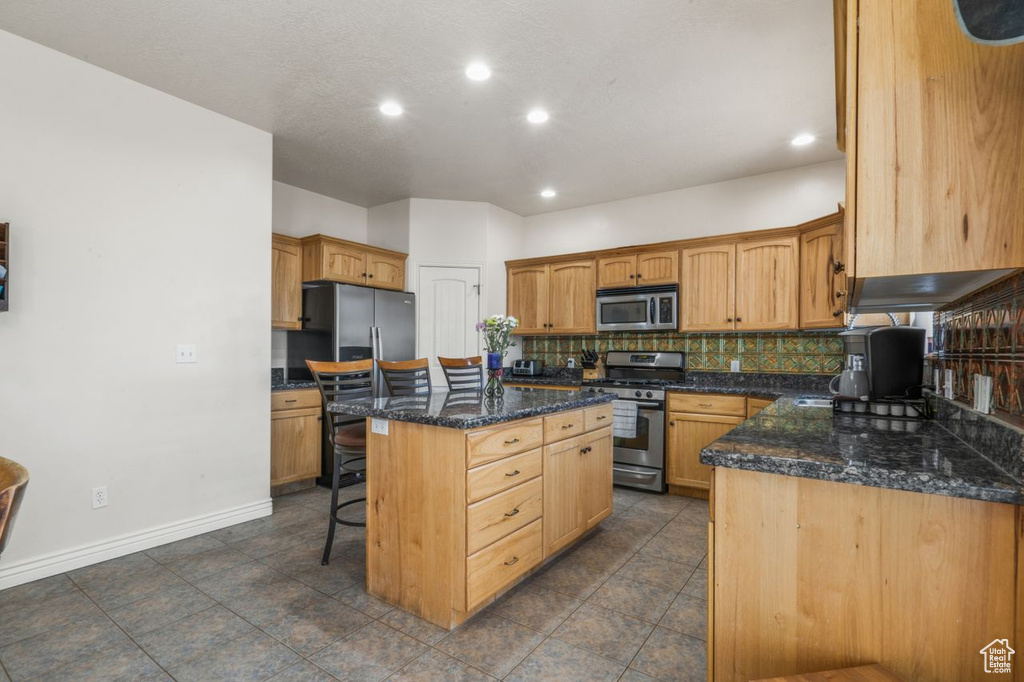 Kitchen featuring a kitchen island, a breakfast bar, dark tile flooring, backsplash, and stainless steel appliances