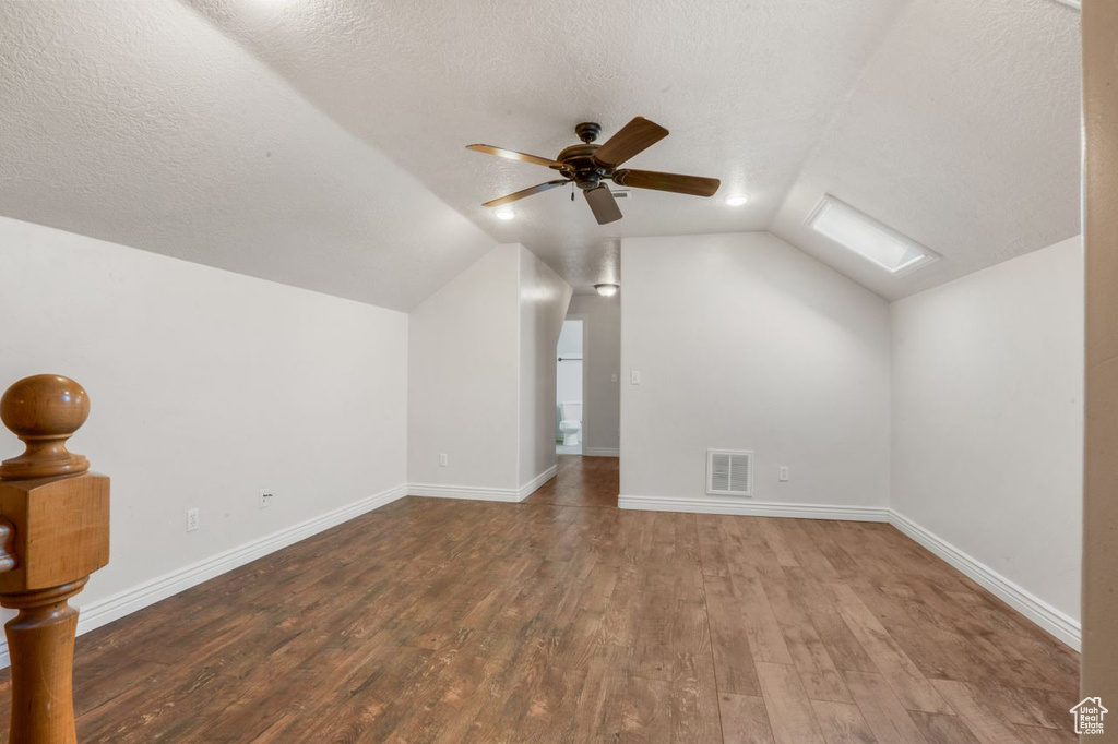 Bonus room with ceiling fan, dark hardwood / wood-style flooring, vaulted ceiling with skylight, and a textured ceiling