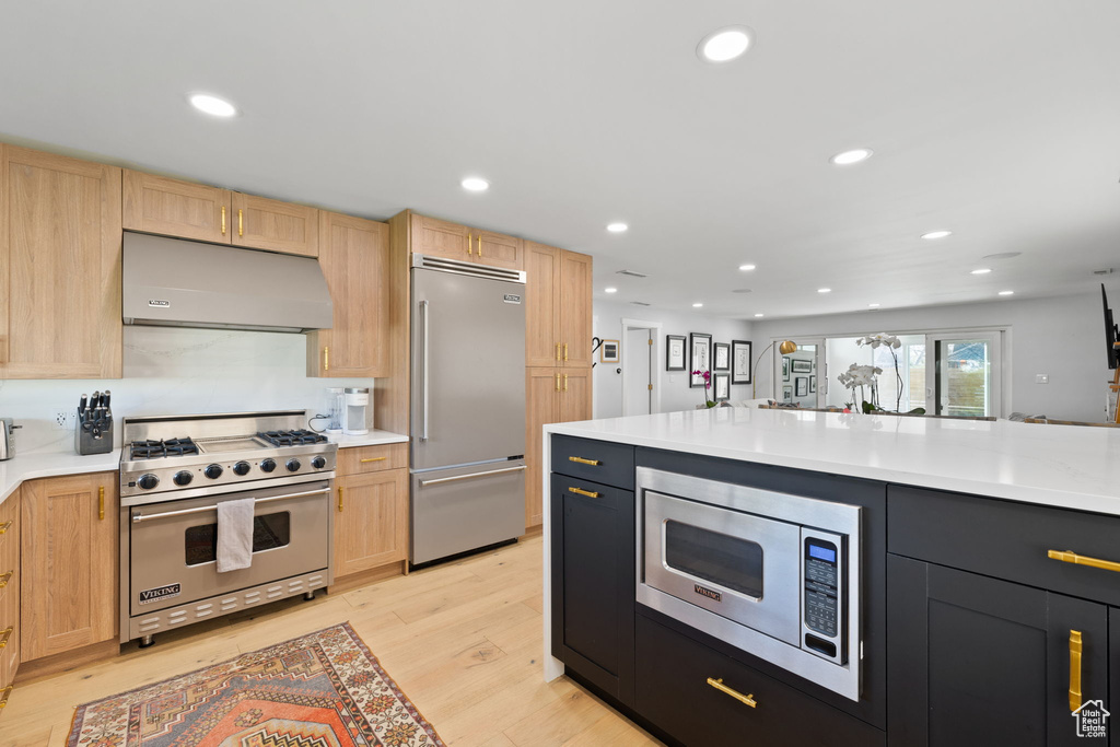 Kitchen featuring light brown cabinetry, built in appliances, and light wood-type flooring