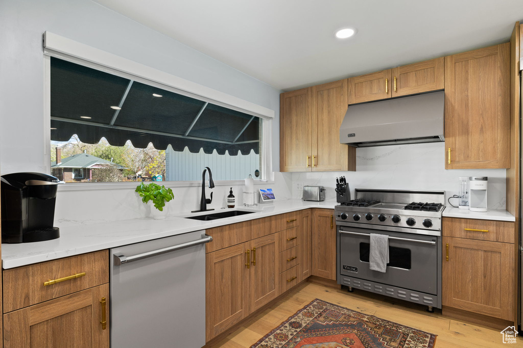 Kitchen with sink, appliances with stainless steel finishes, light hardwood / wood-style flooring, and light stone counters