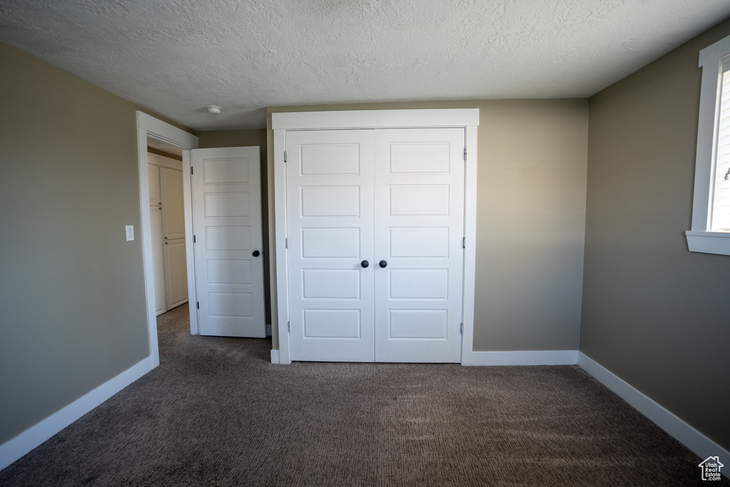 Unfurnished bedroom with dark carpet, a closet, and a textured ceiling