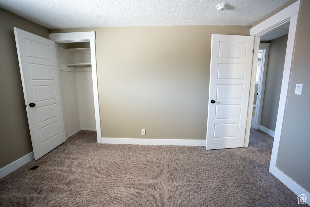Unfurnished bedroom with a closet, a textured ceiling, and dark carpet