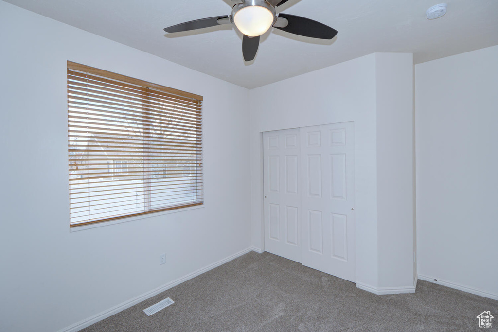 Unfurnished bedroom with a closet, ceiling fan, and dark carpet