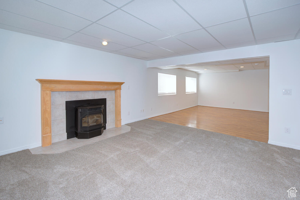 Unfurnished living room with light hardwood / wood-style floors, a wood stove, a paneled ceiling, and a tiled fireplace