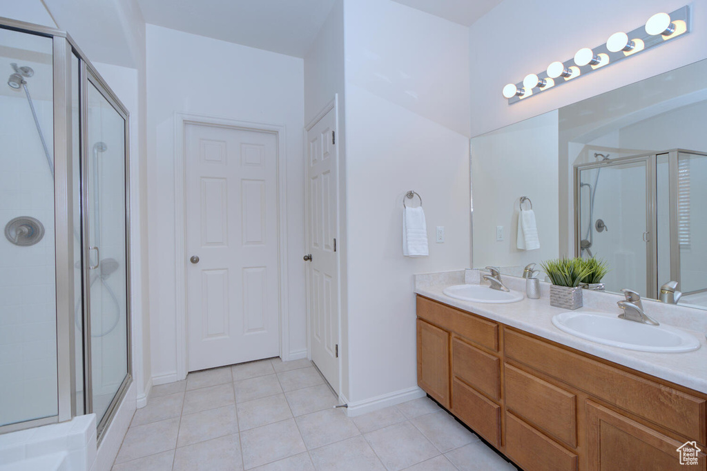 Bathroom with tile flooring, walk in shower, vanity with extensive cabinet space, and double sink