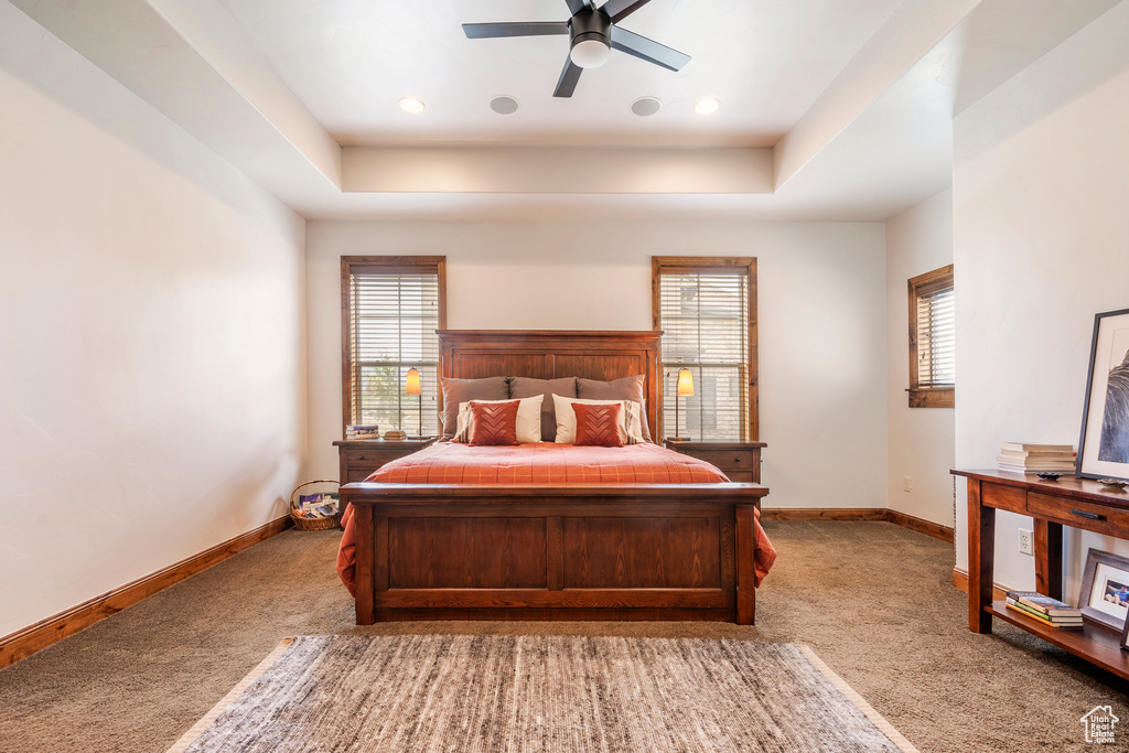 Bedroom with ceiling fan, light carpet, and a tray ceiling
