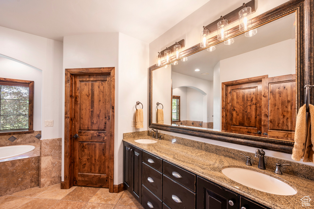 Bathroom featuring tile flooring, dual sinks, vanity with extensive cabinet space, and tiled bath