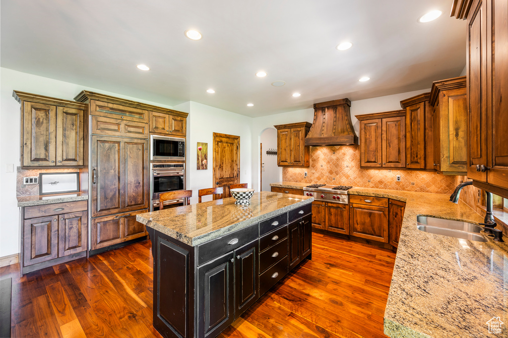 Kitchen with premium range hood, backsplash, stainless steel appliances, dark hardwood / wood-style flooring, and a center island
