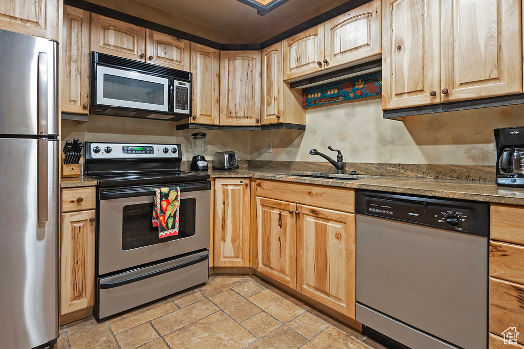 Kitchen with sink, appliances with stainless steel finishes, light tile floors, and dark stone counters
