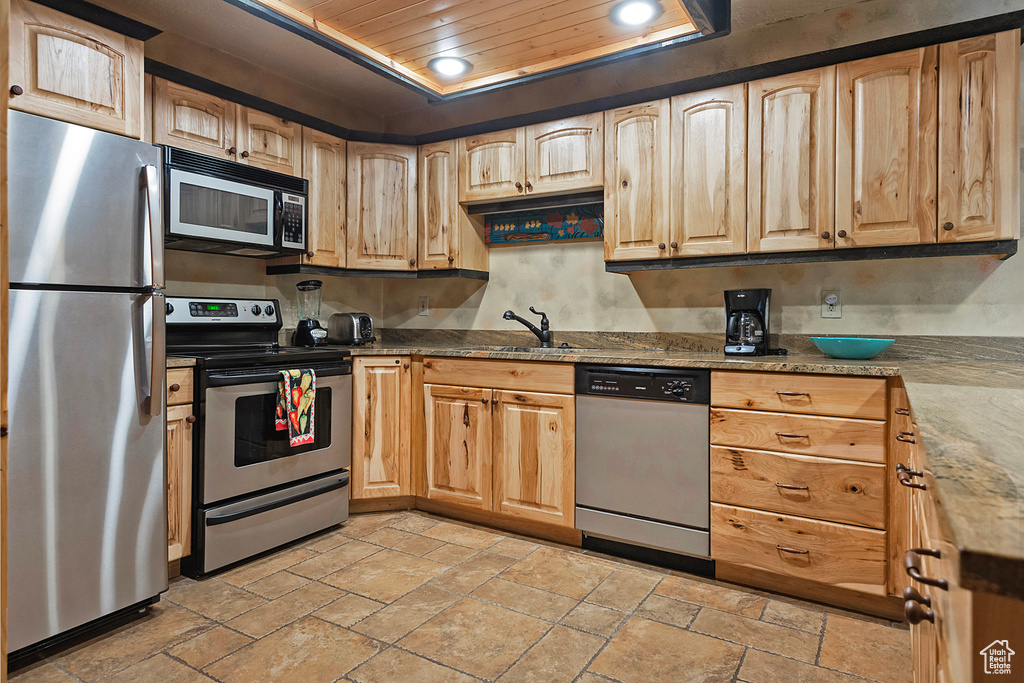 Kitchen with appliances with stainless steel finishes, light tile flooring, light stone counters, wooden ceiling, and sink