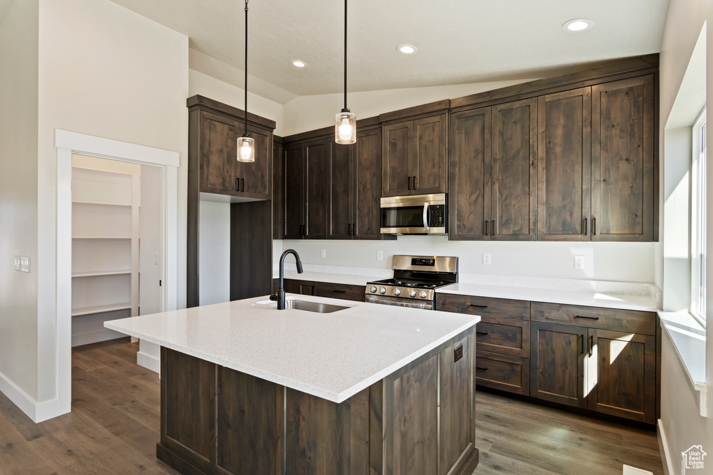 Kitchen with dark brown cabinetry, appliances with stainless steel finishes, sink, dark wood-type flooring, and a center island with sink