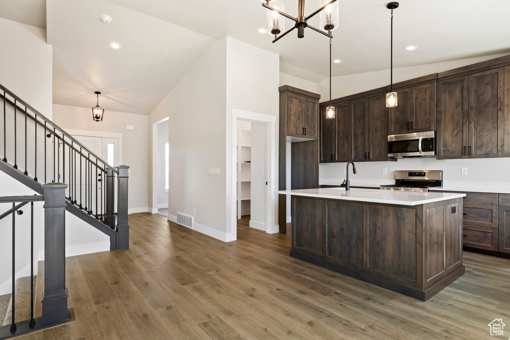 Kitchen featuring stainless steel appliances, dark brown cabinetry, hardwood / wood-style floors, and hanging light fixtures