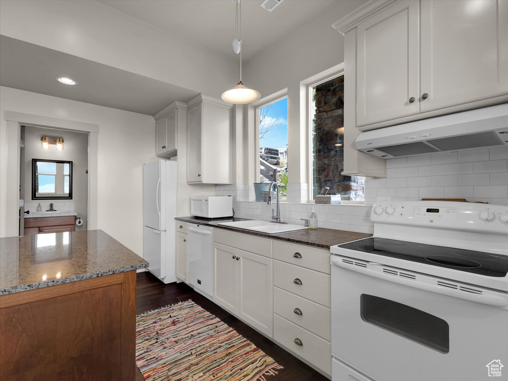 Kitchen with white appliances, tasteful backsplash, dark wood-type flooring, dark stone counters, and white cabinetry