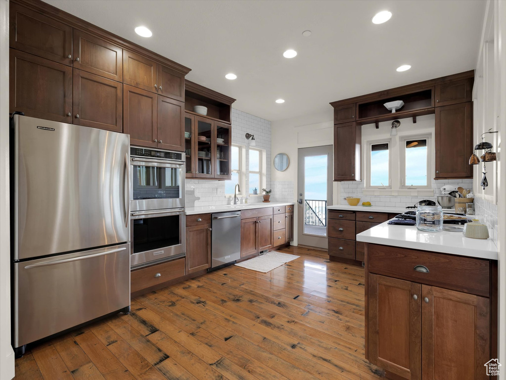 Kitchen featuring backsplash, appliances with stainless steel finishes, dark brown cabinetry, and hardwood / wood-style floors