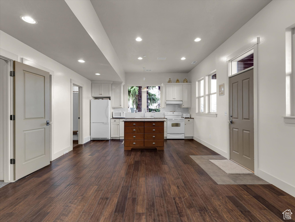 Kitchen featuring white appliances, dark hardwood / wood-style floors, white cabinets, sink, and a center island