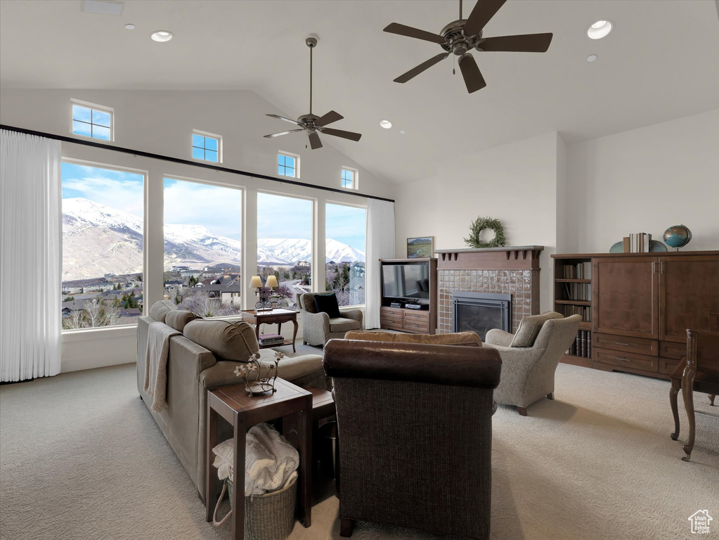 Living room featuring a mountain view, light carpet, high vaulted ceiling, a fireplace, and ceiling fan