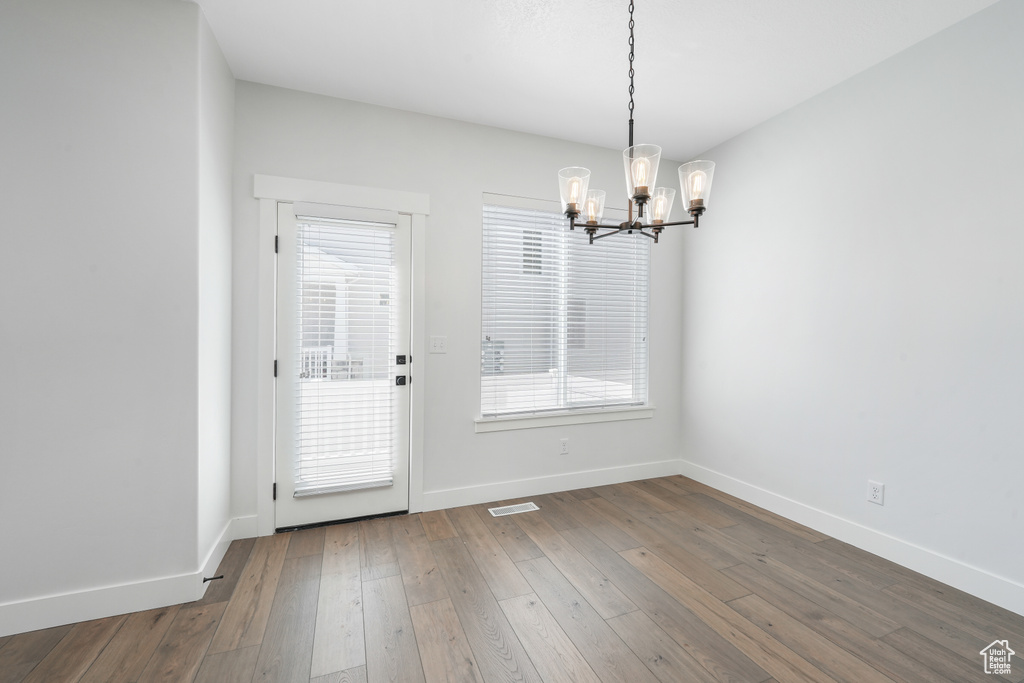 Empty room featuring a healthy amount of sunlight, dark hardwood / wood-style flooring, and an inviting chandelier