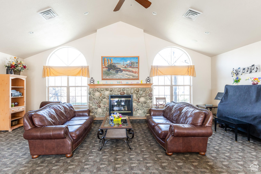 Carpeted living room featuring a stone fireplace, ceiling fan, and lofted ceiling