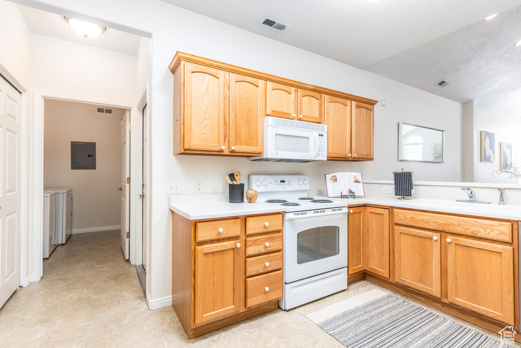 Kitchen with white appliances, sink, light tile floors, and washing machine and clothes dryer
