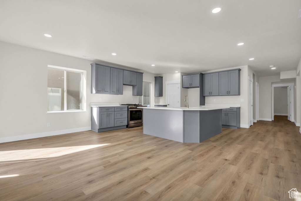 Kitchen featuring gray cabinets, a center island with sink, stainless steel range with gas cooktop, and light wood-type flooring