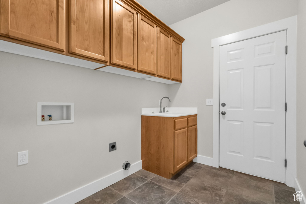 Clothes washing area with electric dryer hookup, dark tile flooring, cabinets, and sink