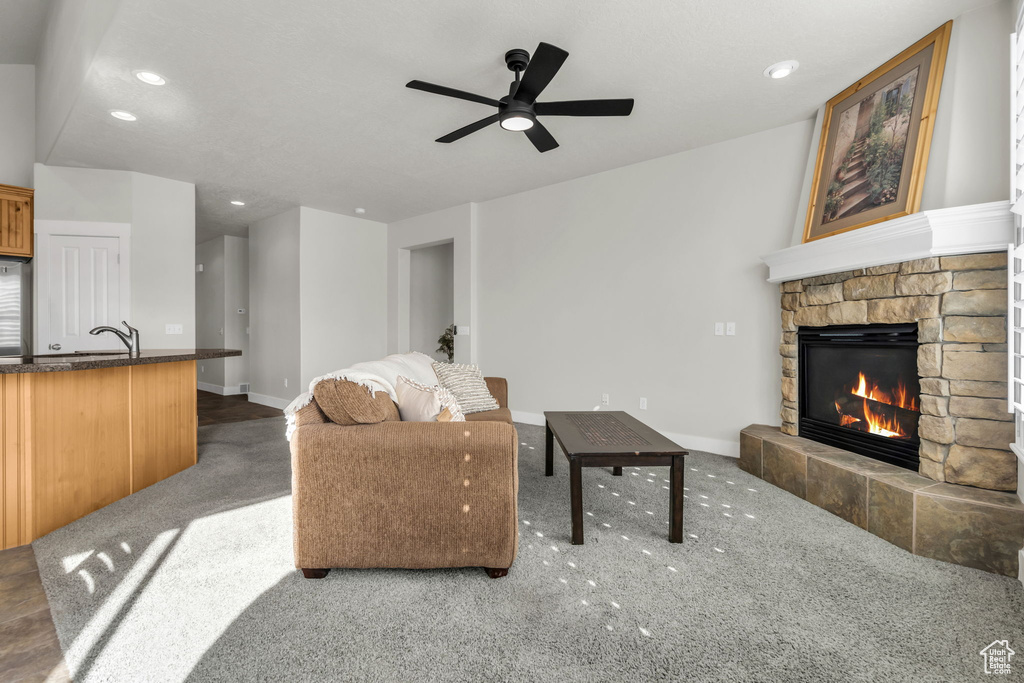 Carpeted living room featuring sink, ceiling fan, and a stone fireplace