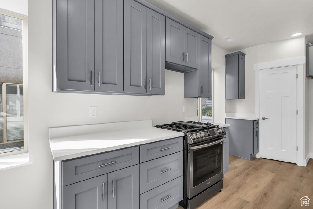 Kitchen with gray cabinets, light hardwood / wood-style flooring, and stainless steel range with gas cooktop