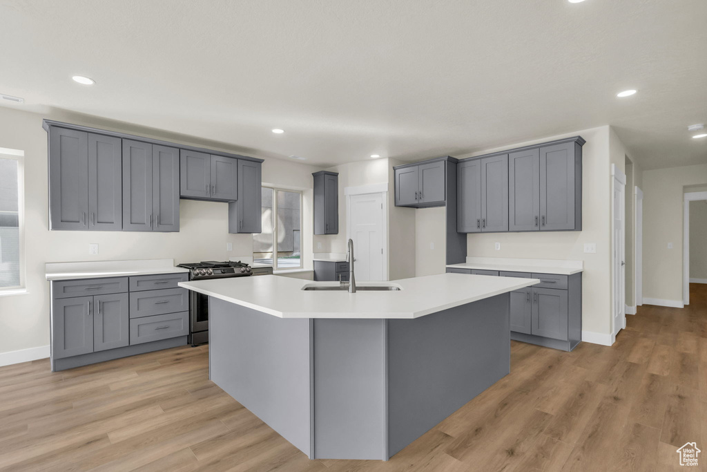 Kitchen with gray cabinetry, an island with sink, gas range, sink, and light wood-type flooring