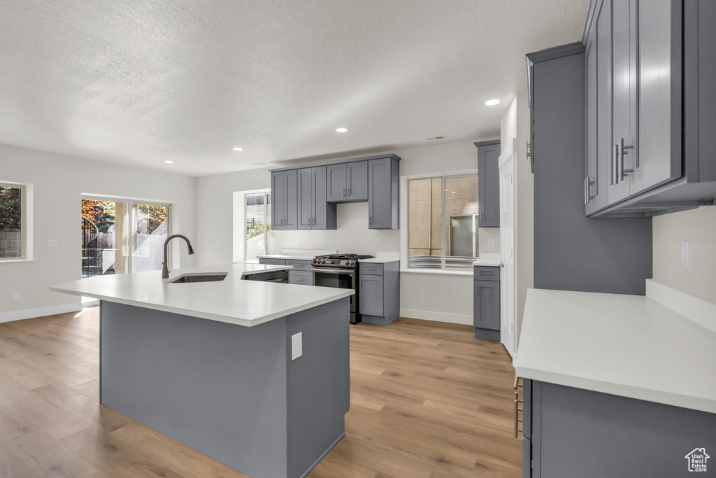 Kitchen featuring light wood-type flooring, gray cabinetry, sink, stainless steel gas range, and an island with sink
