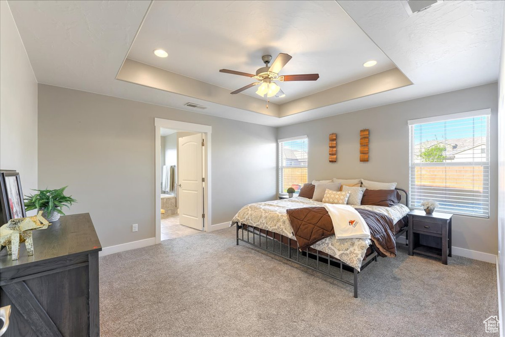 Carpeted bedroom featuring ceiling fan, ensuite bathroom, and a tray ceiling