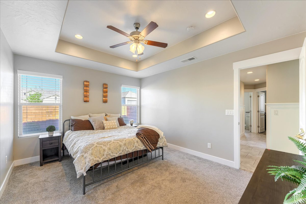 Carpeted bedroom featuring ceiling fan, a raised ceiling, and multiple windows