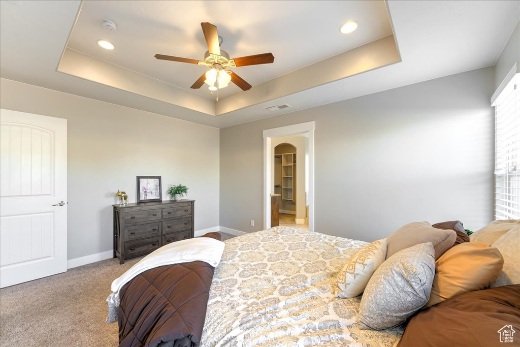 Bedroom featuring light colored carpet, a walk in closet, ceiling fan, and a raised ceiling