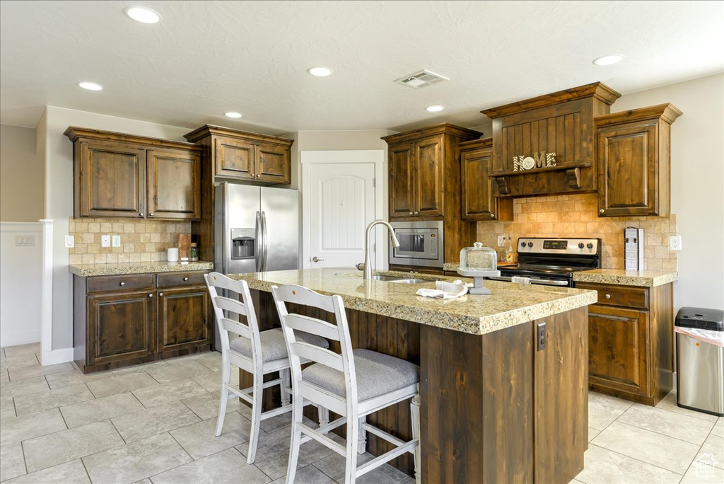 Kitchen with stainless steel appliances, sink, light tile floors, a center island with sink, and tasteful backsplash