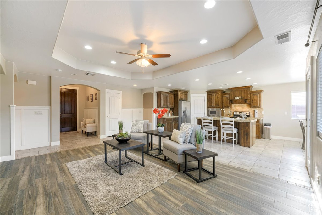 Living room featuring ceiling fan, light tile flooring, and a raised ceiling