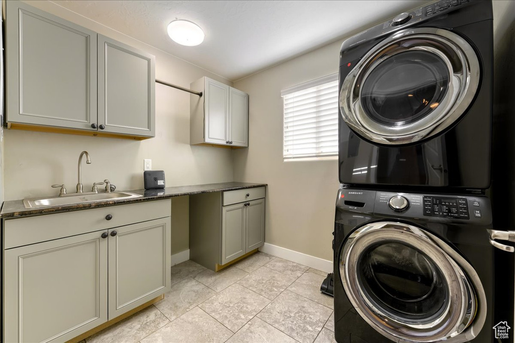 Laundry room with sink, stacked washing maching and dryer, cabinets, and light tile floors