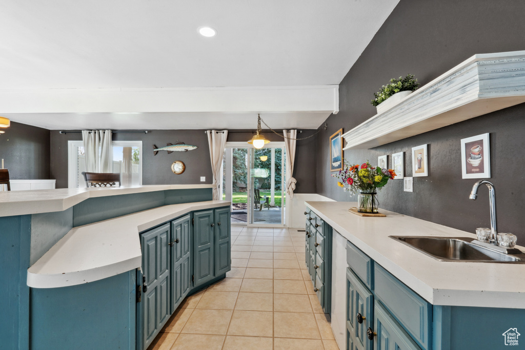 Kitchen with pendant lighting, light tile flooring, sink, a kitchen island, and blue cabinets