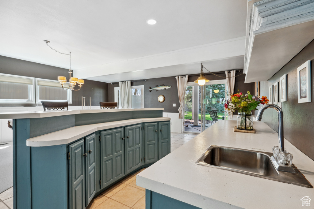 Kitchen featuring light tile flooring, an island with sink, sink, pendant lighting, and an inviting chandelier